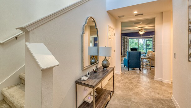 A hallway with a staircase, a console table with a lamp, a mirror, and a view into a dining area with a chair and table. - Brand New, Stylish 4-Bed 3-Bath Home. Conservation Views & Gated Resort Amenities. Near Disney! (Davenport)