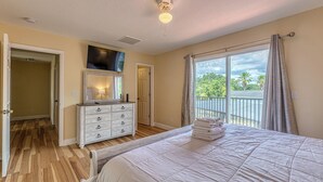 Une chambre à coucher comprenant un lit, une commode, un téléviseur fixé au mur et un balcon avec des rideaux.