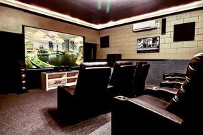 A home theater with leather reclining chairs, a large flat-screen TV, and a cityscape view.