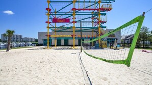 A beach volleyball court with a net, yellow and green poles, and a building in the background. - A · New 4Br King Beds Steps to Beach &2nd Pier #A (Myrtle Beach)
