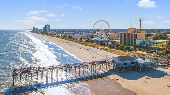 Una playa con un muelle, una noria y edificios al fondo.