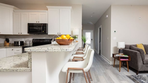 Una cocina moderna con armarios blancos, encimera de granito y una isla central con taburetes de bar.