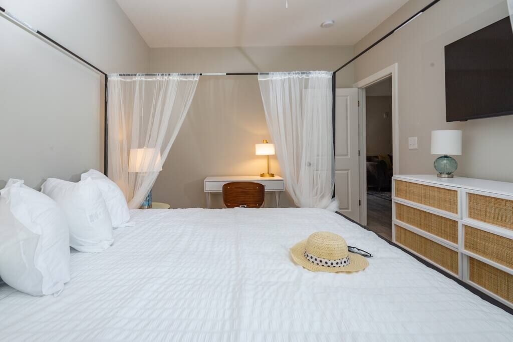 A hotel room with a bed, a desk, a chair, a bedside table with a lamp, a wardrobe, and a TV mounted on the wall.