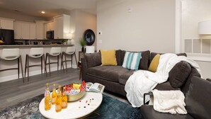 Una sala de estar moderna con un sofá, una mesa de centro con aperitivos y una cocina al fondo.