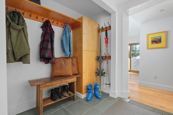 Un couloir avec un porte-manteau, un banc et des bottes.
