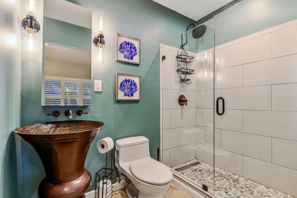 A bathroom with a large copper sink, white toilet, and a glass-enclosed shower with white tiles.