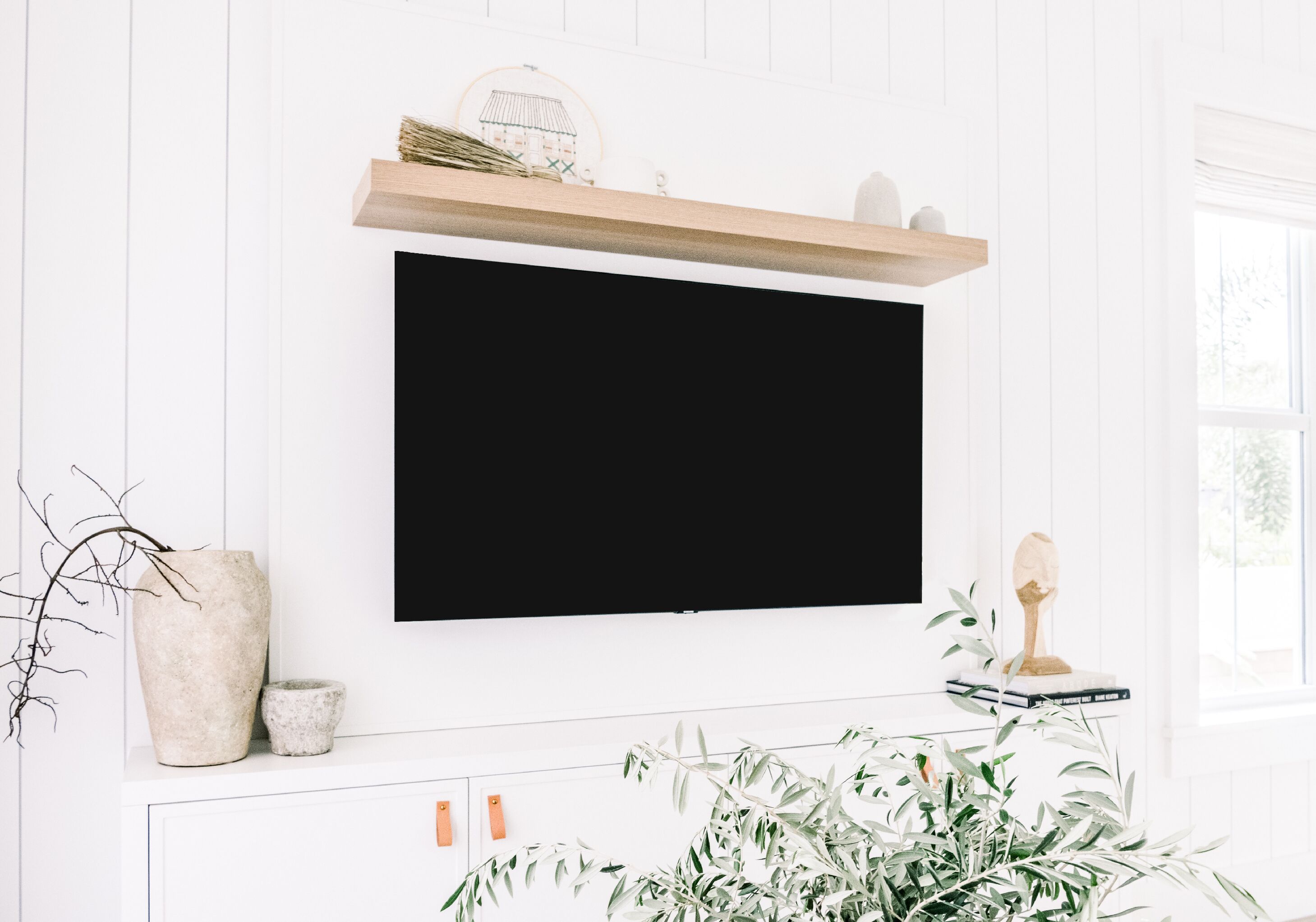 Un salon avec un téléviseur fixé au mur, un vase en pierre, une petite plante et une étagère en bois ornée d’objets décoratifs.