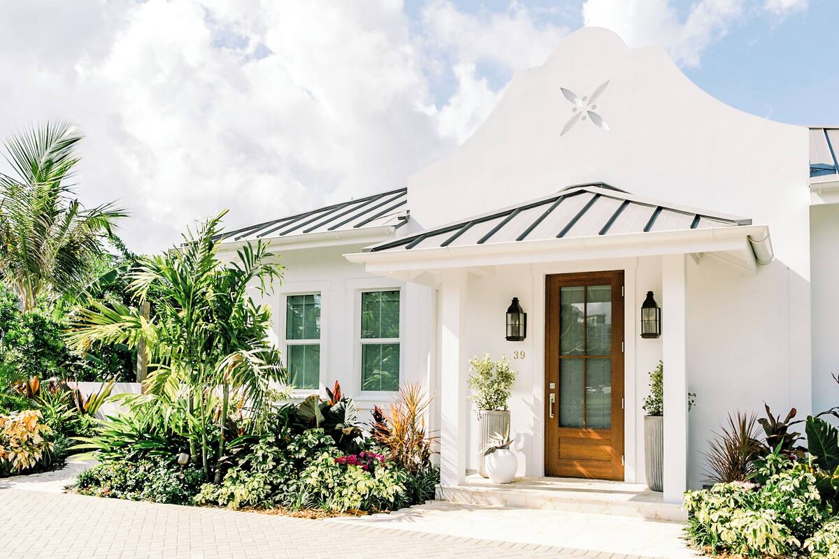 A white building with a wooden door, a star-shaped window, and a garden with various plants.