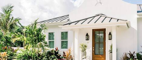 Un edificio blanco con puerta de madera, una ventana en forma de estrella y un jardín con diversas plantas.
