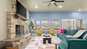 A living room with a stone fireplace, a green sofa, yellow armchairs, and a large window offering a view of the outdoors.