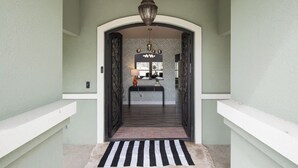 A hallway with a black and white striped rug leading to a room with a patterned wall and a black-framed mirror.