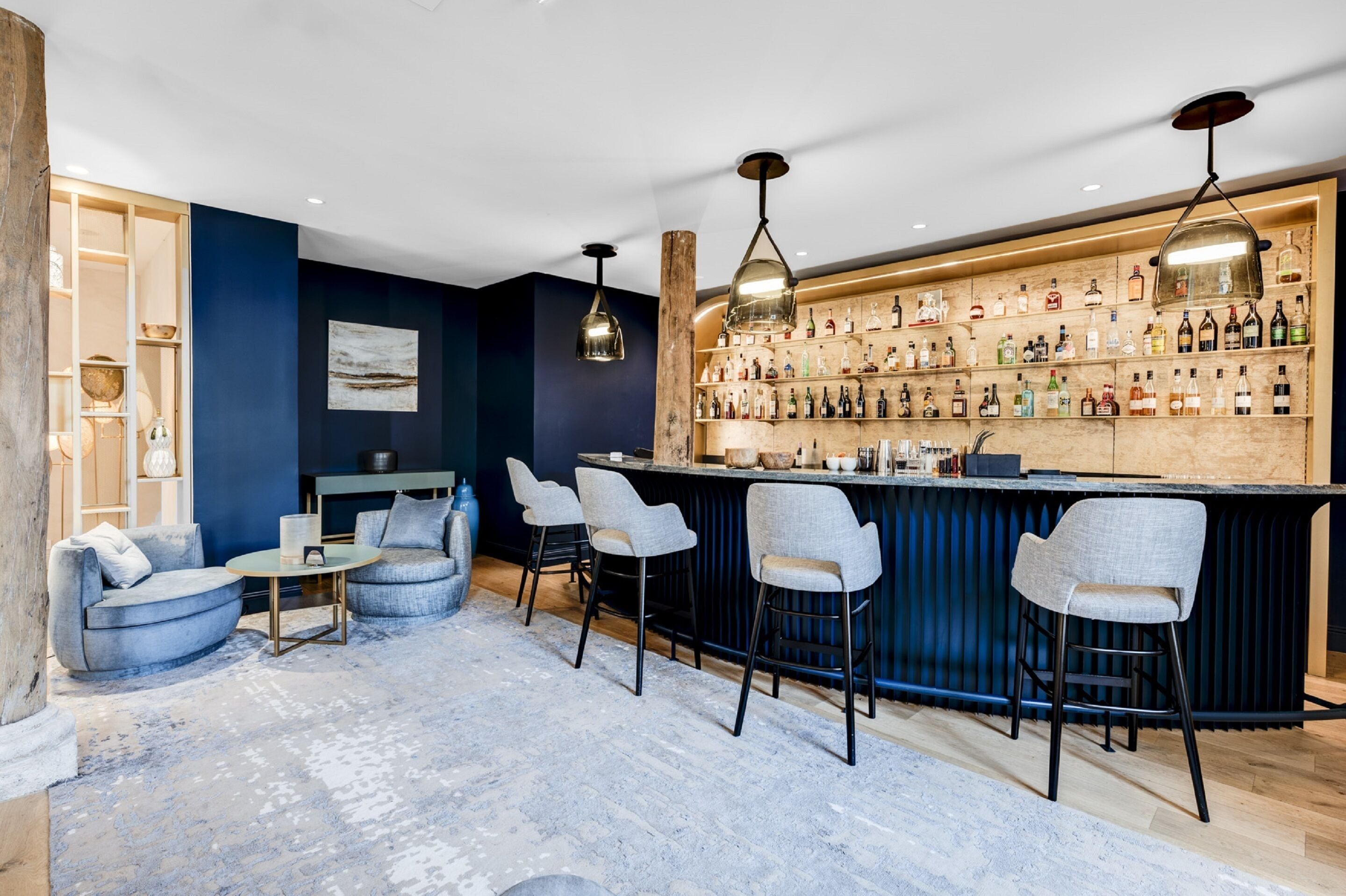 A bar area with a wooden bar counter, multiple bar stools, and a variety of bottles on shelves.