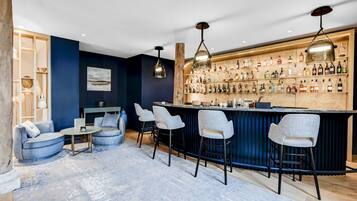 A bar area with a wooden bar counter, multiple bar stools, and a variety of bottles on shelves.