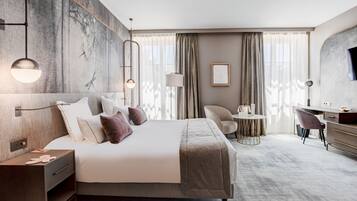 Una habitación de hotel moderna con una cama grande, mesitas de noche, un escritorio, una silla y un televisor.