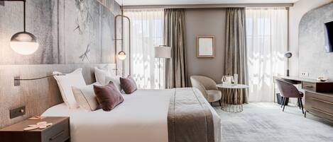 Una habitación de hotel moderna con una cama grande, mesitas de noche, un escritorio, una silla y un televisor.