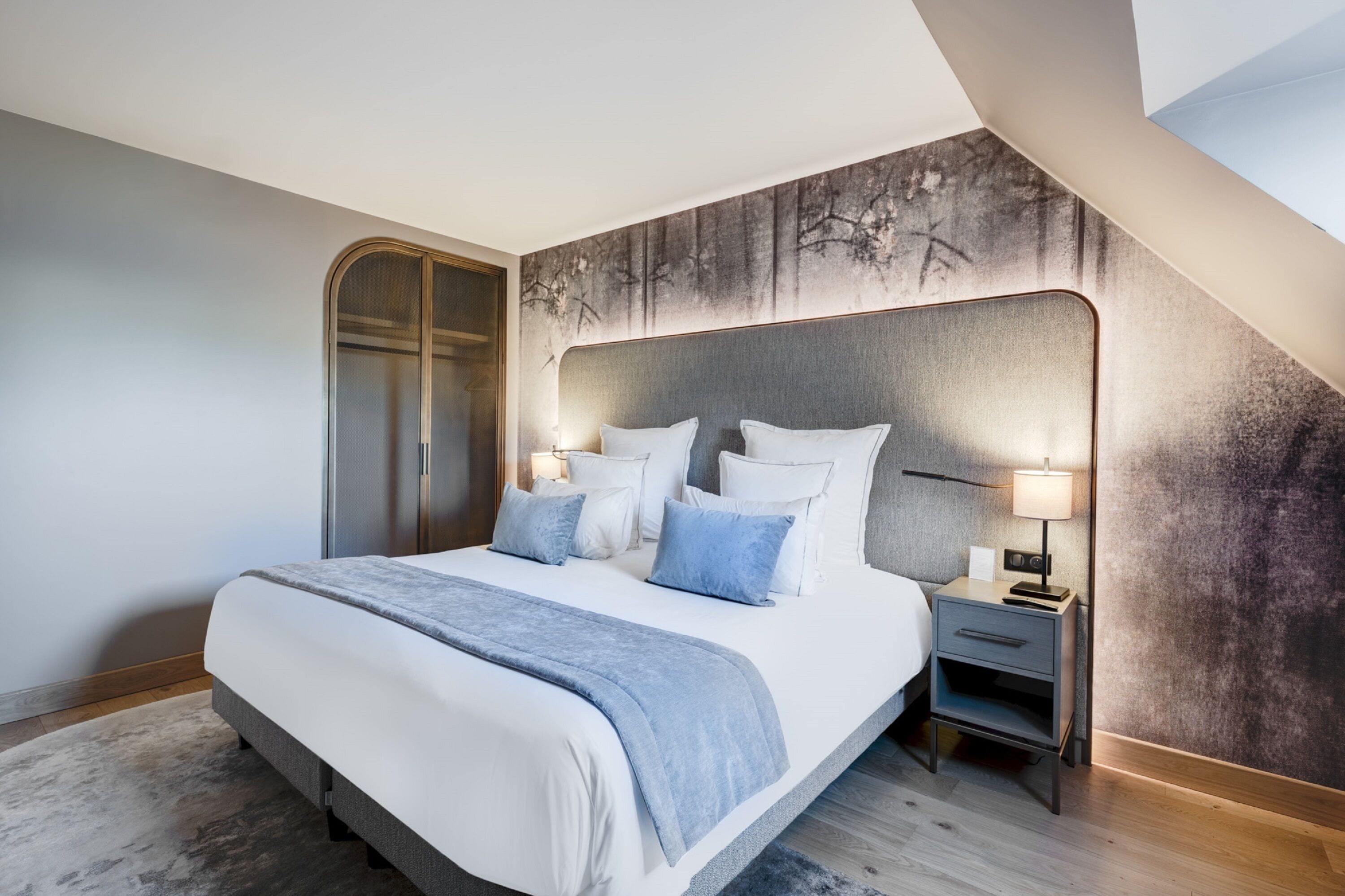 A modern bedroom with a large bed, a nightstand, and a headboard with a textured wall behind it.
