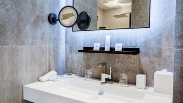 A modern bathroom with a large mirror, a white sink, and a shelf with toiletries.