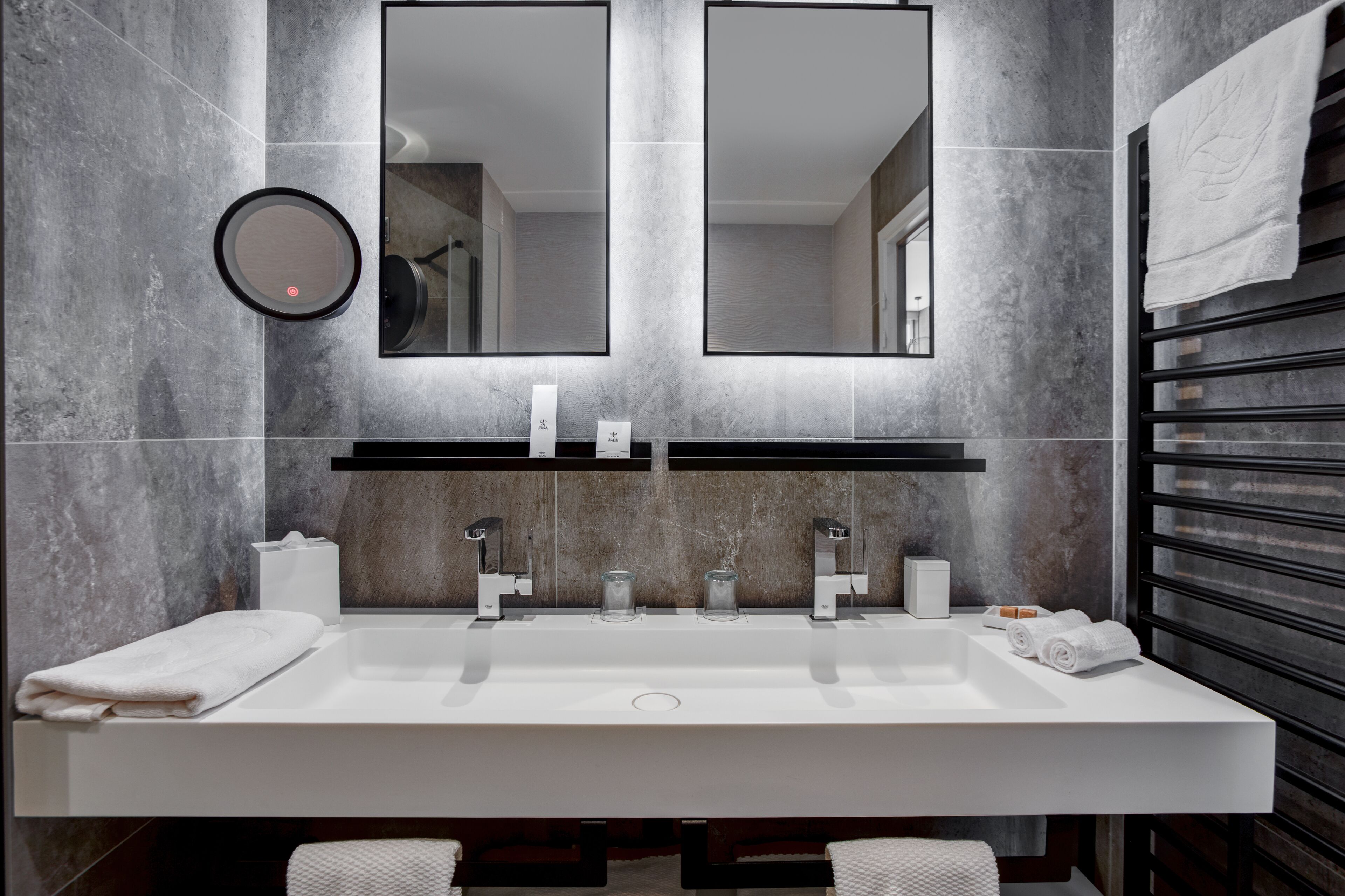 A modern bathroom with a large sink, two mirrors, and a towel rack.