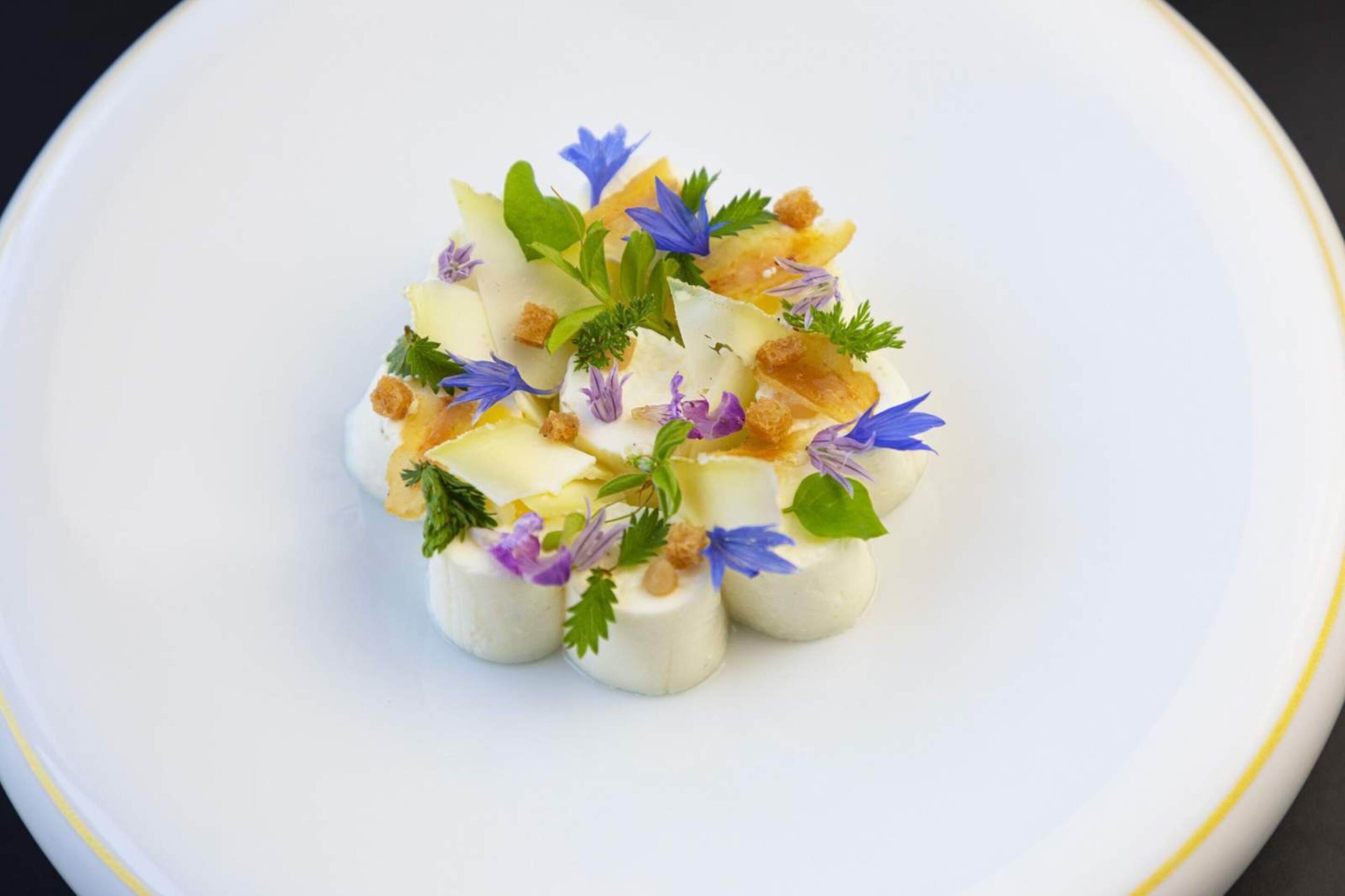 A white plate with a food arrangement featuring small, round, white items topped with purple flowers and green leaves.