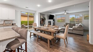 A spacious living area with a wooden dining table, comfortable seating, a fireplace, and a television mounted on the wall.