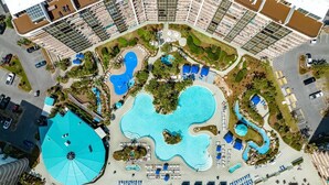 Ein Resort mit mehreren Schwimmbecken, darunter ein großes zentrales Becken und ein kreisförmiges Becken mit einem blauen Dach.