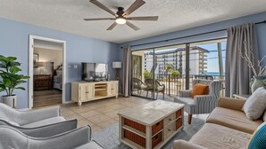 Ein geräumiges Wohnzimmer mit Deckenventilator, Fernseher und Balkon mit Gartenmöbeln.