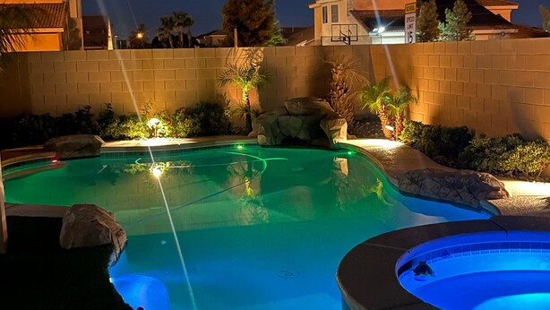 A swimming pool with a hot tub, surrounded by a brick wall and various plants. - CasAHermosa GetAway (North Las Vegas)