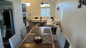 A modern kitchen with a dining area, featuring a wooden table with placemats, a refrigerator, and a ceiling fan. - CasAHermosa GetAway (North Las Vegas)