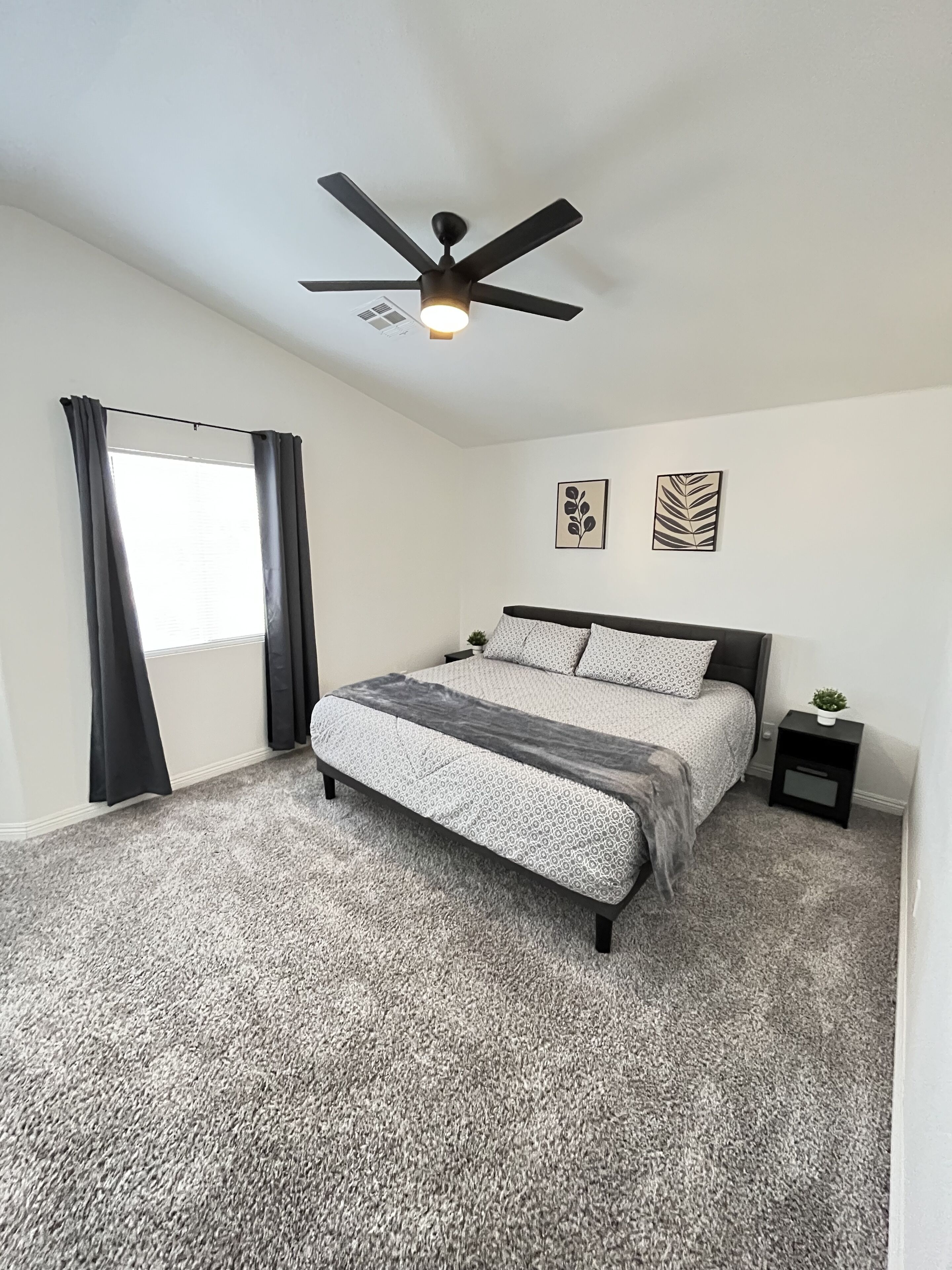 A bedroom with a bed, a ceiling fan, a nightstand, and two wall art pieces.