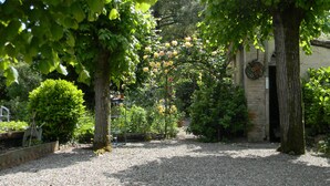 A gravel pathway leading to a building with a stone facade, surrounded by lush greenery and trees.