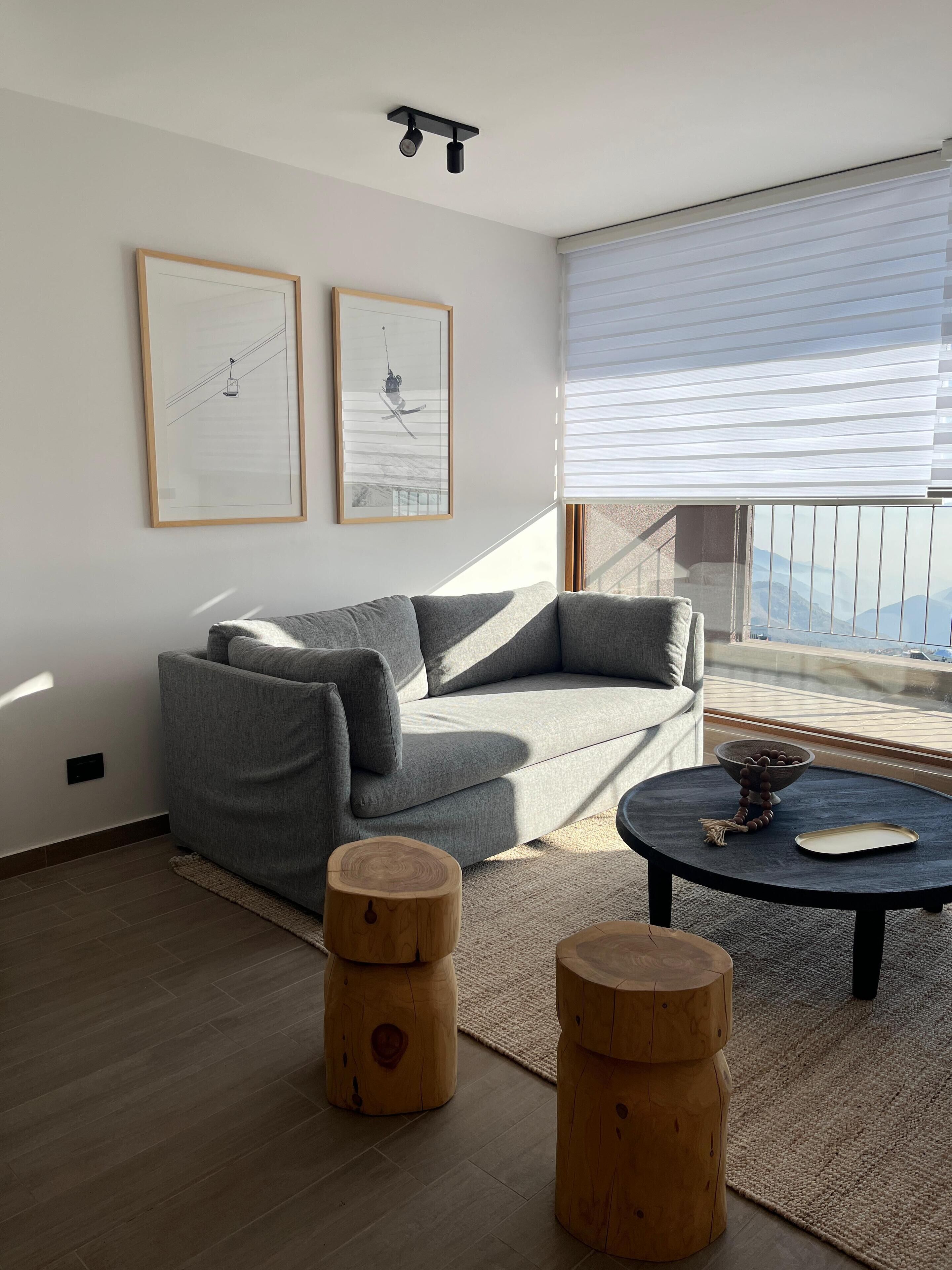 A modern living room with a grey sofa, two wooden stools, a round coffee table, and two framed artworks on the wall.