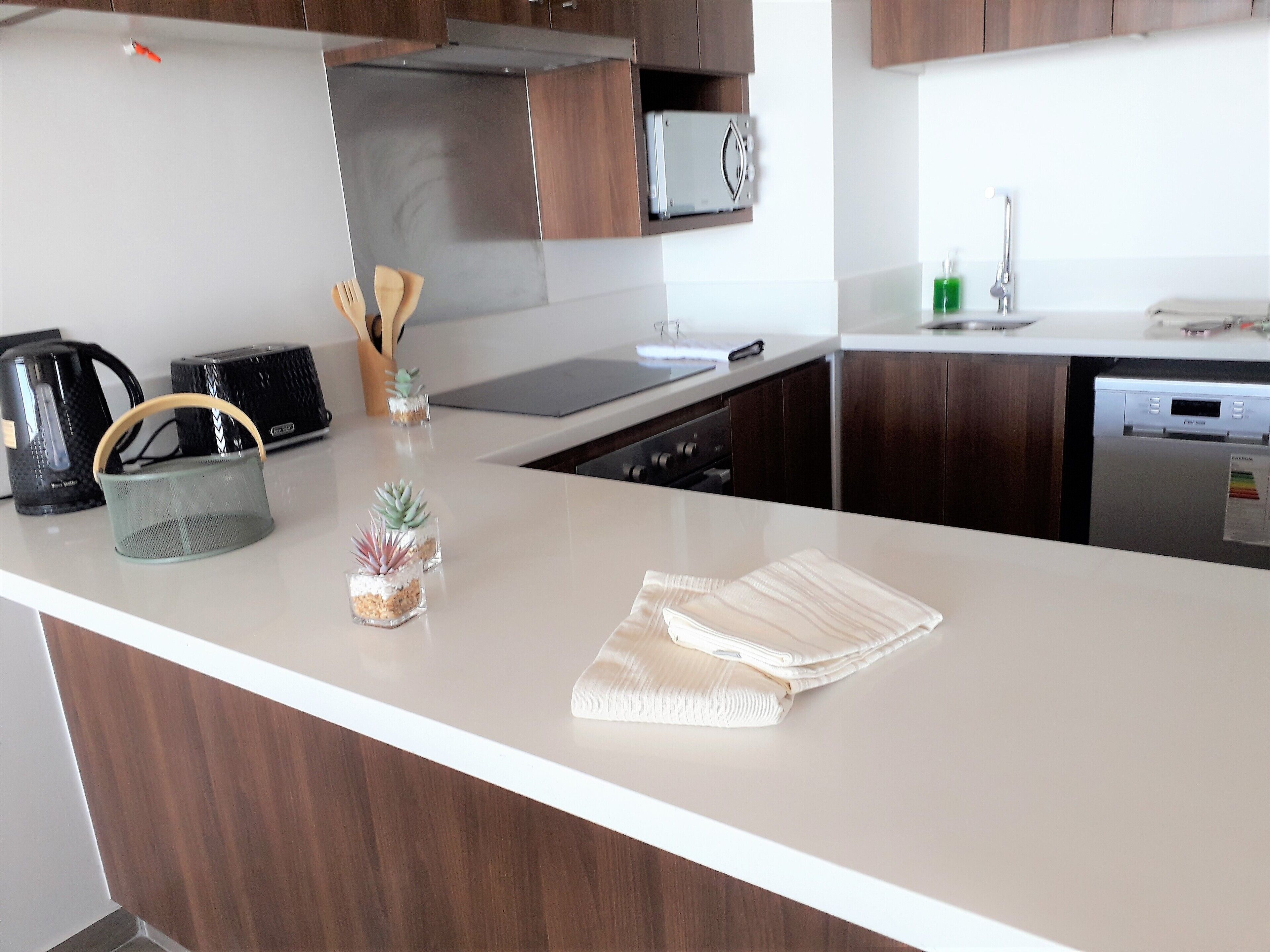 Une cuisine moderne avec des meubles en bois, des appareils en acier inoxydable et un plan de travail blanc.
