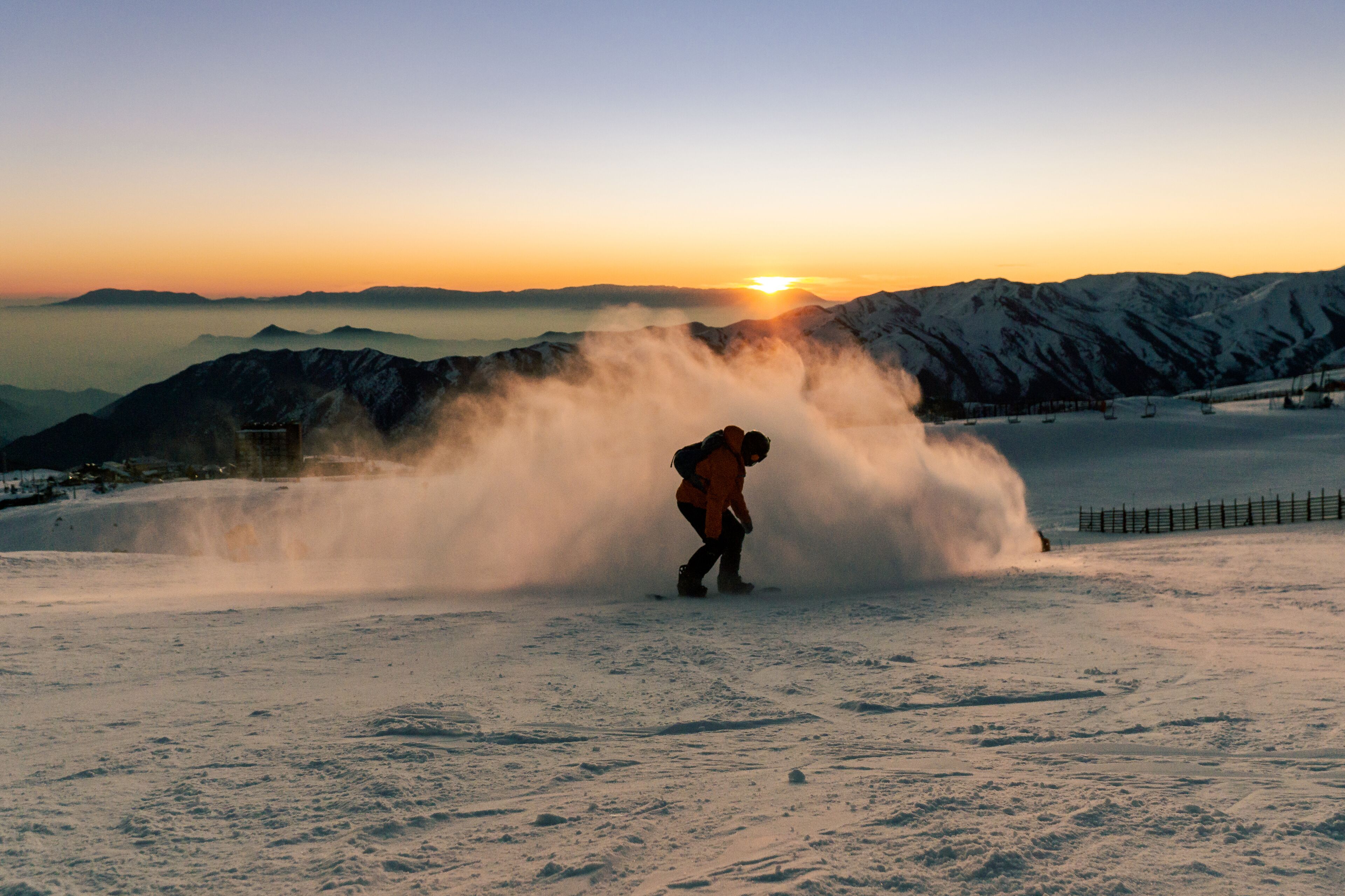 A snowboarder in a snowy landscape with a mountain backdrop and a setting sun.