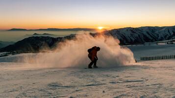 A snowboarder in a snowy landscape with a mountain backdrop and a setting sun.