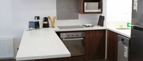 A modern kitchen with wooden cabinets, a white countertop, a microwave, a toaster, and a dishwasher.