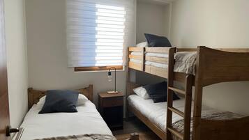 A bunk bed room with a window, a bedside table, and a lamp.