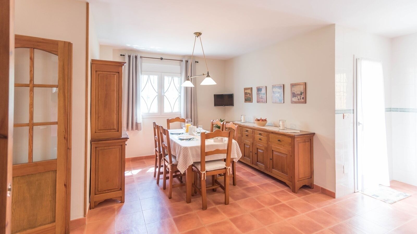A dining area with a wooden table and chairs, a kitchen with wooden cabinets, and a window with curtains.