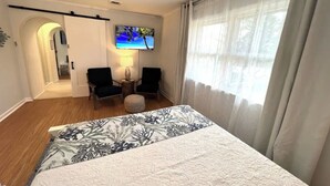 Habitación de hotel con cama, dos sillas, una mesita, televisor y ventana con cortinas.