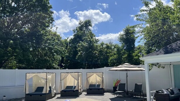 En trädgård med en pool, solstolar och en möblerad uteplats under tak.