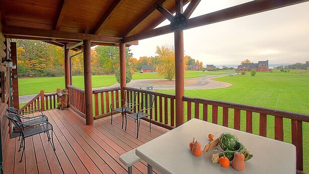 A covered outdoor deck with wooden railings, a table with pumpkins, and chairs. - Twin Chalets of Finger Lakes (Geneva)