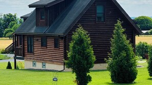 A wooden cabin with a sloped roof, a balcony, and a well-maintained lawn with two evergreen trees. - Twin Chalets of Finger Lakes (Geneva)