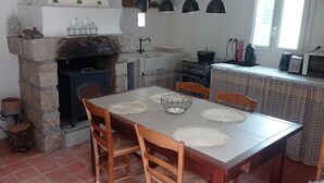 Eine gemütliche Küche mit Kamin aus Stein, einem Holzespeisetisch und modernen Geräten.