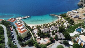 Oversigtsbillede af en kystferie med flere bygninger, en strand og en swimmingpool.