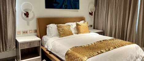A hotel room with a large bed, two bedside tables, a wall-mounted artwork, and curtains.