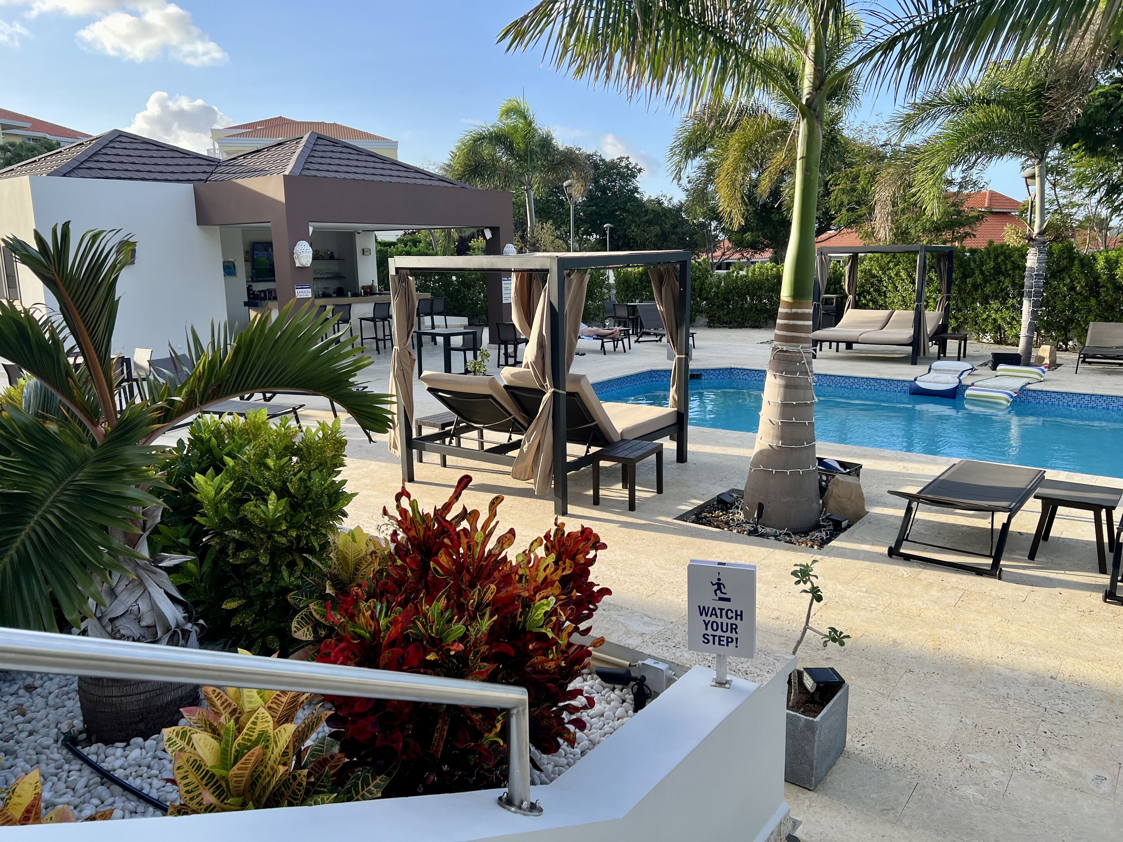 Un espace aménagé au bord de la piscine, avec des chaises longues, une piscine et un panneau indiquant une zone où il faut faire attention en marchant.