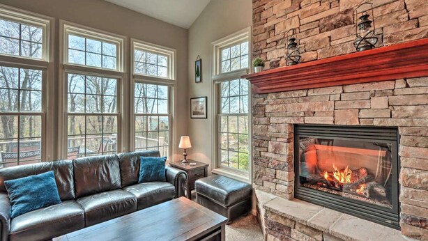 A living room with a stone fireplace, leather sofa, and large windows.