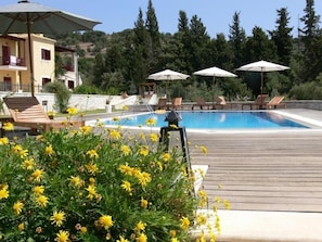 A pool area with lounge chairs and umbrellas, surrounded by a wooden deck and yellow flowers.