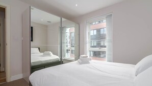 A hotel room with a large bed, a mirror, and a window with blinds.
