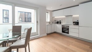 A modern kitchen with white cabinets, a glass dining table, and a view of the outside.
