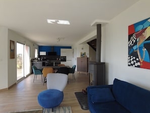 Una sala de estar moderna con un sofá azul, una zona de comedor con sillas, una cocina con armarios blancos y un cuadro grande en la pared.